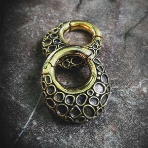 Può includere: Due gauge per orecchie in metallo color oro con un design circolare testurizzato. Le gauge sono impilate l'una sull'altra.