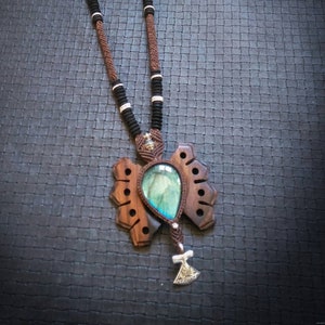 Peut inclure: Un collier en cordon brun et noir avec un pendentif en bois orné d'une pierre précieuse bleue et d'un charme de hache argenté.