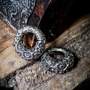 May include: Two silver hoop earrings with a textured, organic design. The earrings are on a wooden surface.