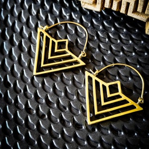 May include: A pair of gold geometric hoop earrings with a triangular design. The earrings are made of a thin metal wire and have a simple, modern look.