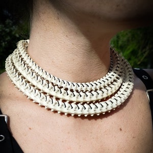 Peut inclure: Un collier en os blanc à plusieurs rangs, porté autour du cou d'une personne. Le collier est composé de petites pièces d'os individuelles qui sont reliées entre elles.