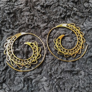 Peut inclure: Une paire de boucles d'oreilles créoles en spirale dorées avec des motifs complexes. Les boucles d'oreilles sont en métal fin et ont un style bohème délicat.