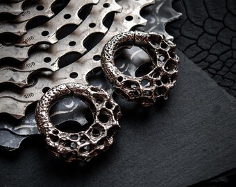 May include: Two silver earrings with a textured, organic design. The earrings are on a black surface.