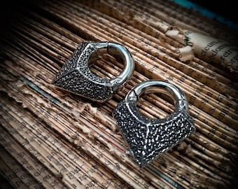 May include: Two silver-toned, textured, circular, hinged earrings with a triangular shape on each side. The earrings are on a textured, brown surface.