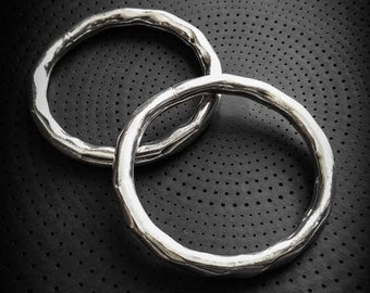 May include: Two silver rings with a hammered texture, stacked on top of each other, on a black background with a repeating pattern of small circles.