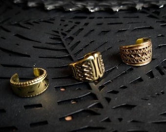 Puede incluir: Tres pendientes de oreja dorados con intrincados diseños geométricos. Los pendientes están sobre un fondo negro.