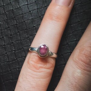 Peut inclure: Une bague en argent avec une pierre ovale rose. La bague est sur le doigt d'une personne.