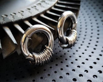 May include: Two silver hoop earrings with a coiled design. The earrings are on a black surface with a pattern of small holes.