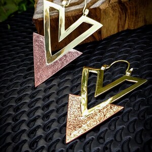 Peut inclure: Une paire de boucles d'oreilles triangulaires en or et cuivre avec une texture martelée. Les boucles d'oreilles sont grandes et ont un design géométrique.