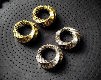 Puede incluir: Cuatro anillos de metal, dos de oro y dos de plata, con un diseño geométrico retorcido. Los anillos están sobre una superficie negra texturizada.