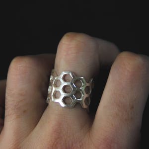 Peut inclure: Une bague en argent avec un motif en nid d'abeille. La bague est portée au doigt.