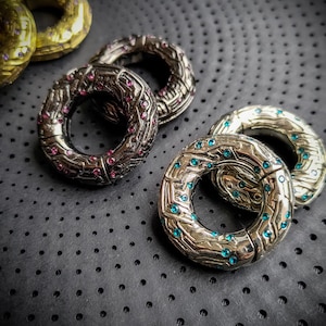 Peut inclure: Quatre anneaux en argent avec des motifs complexes et des pierres précieuses colorées. Les anneaux sont empilés sur une surface noire avec un motif en pointillés.