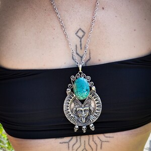 May include: A silver necklace with a turquoise stone pendant featuring a detailed skull and face design. The pendant is surrounded by smaller skulls.