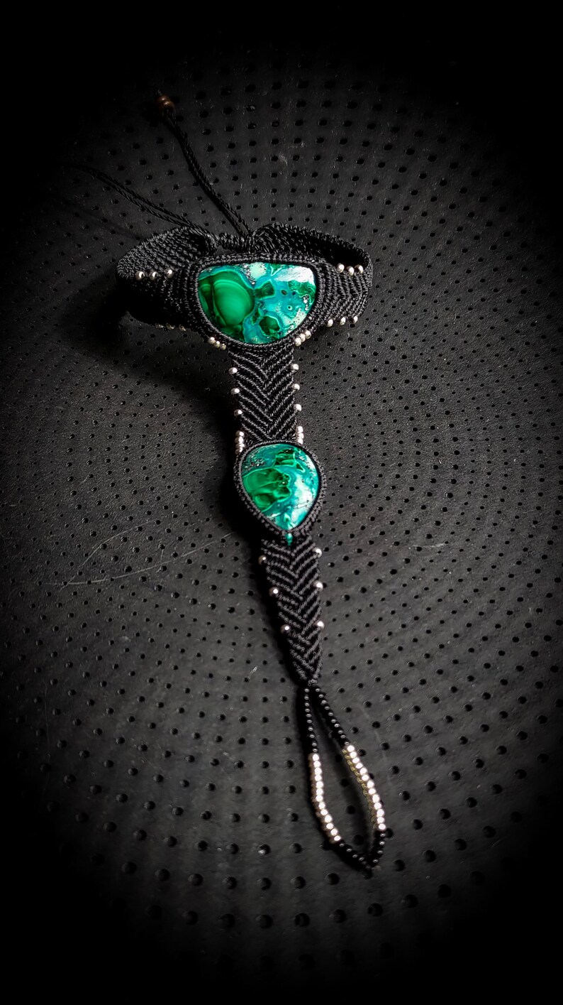 May include: A black macrame ankle bracelet with two green malachite stones. The bracelet is tied with a knot at the ankle and has silver beads throughout.