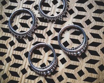 May include: Four silver hoop earrings with beaded edges, displayed on a wooden surface with a geometric pattern.