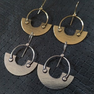 May include: A pair of earrings with a half-circle design. The earrings are made of metal and have a brushed finish. One pair is silver and the other is gold.