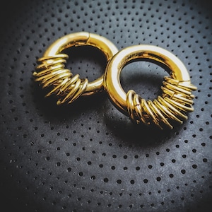 May include: Two gold-coloured metal hoop earrings with a unique design. The hoops are made of multiple rings stacked on top of each other.