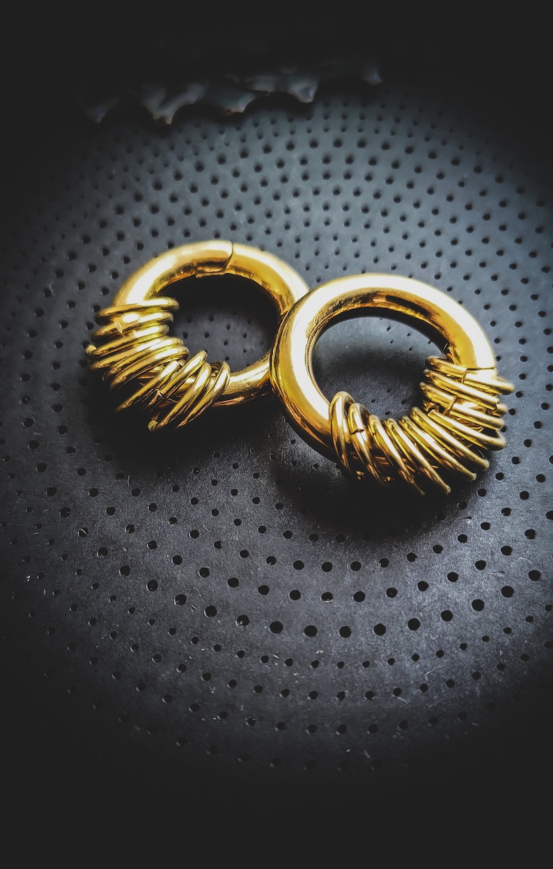 May include: Two gold-coloured metal hoop earrings with a unique design. The hoops are made of multiple rings stacked on top of each other.
