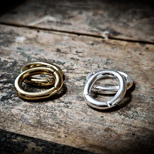 以下が含まれることがあります： 2つのセットの楕円形の金属リング。1つのセットは金色で、もう1つのセットは銀色です。リングは互いに積み重ねられ、木製の表面の上に置かれています。
