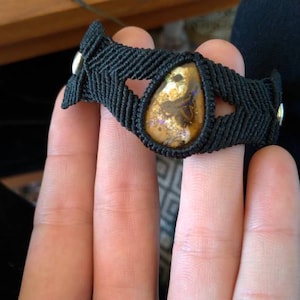 Peut inclure: Un bracelet en cordon noir avec une pierre en forme de larme brune et blanche au centre.