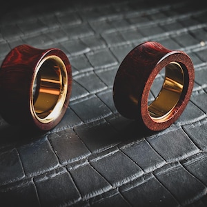 May include: Two wooden ear gauges with a gold metal inlay. The gauges are a dark red colour and have a smooth, polished finish.