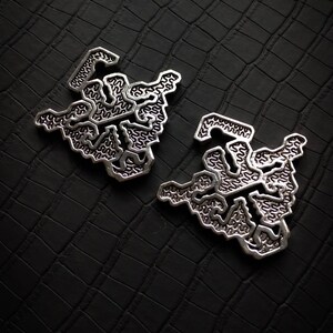 May include: Two silver earrings with a geometric, intricate design. The earrings are on a black textured background.