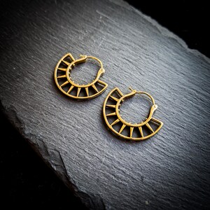 May include: A pair of gold hoop earrings with a geometric sunburst design. The earrings are made of metal and have a shiny finish.