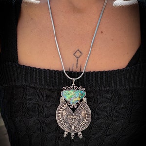 May include: A silver chain necklace with a large pendant featuring a green and blue abalone shell and a silver skull design.