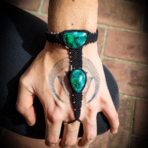 May include: Black macrame bracelet with two green malachite stones. The bracelet is tied around the wrist and has a finger loop.