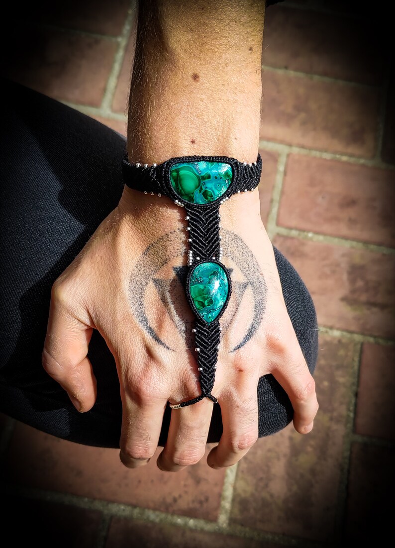 May include: Black macrame bracelet with two green malachite stones. The bracelet is tied around the wrist and has a finger loop.
