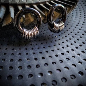 May include: Two black circular rings with silver metal rings stacked on top of each other. The rings are on a black surface with a pattern of small holes.
