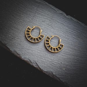 May include: A pair of gold hoop earrings with a geometric design. The earrings are made of metal and have a sunburst pattern.