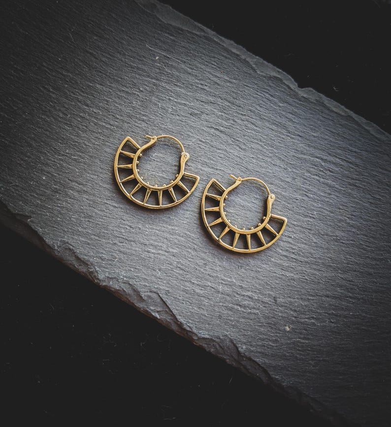 May include: A pair of gold hoop earrings with a geometric design. The earrings are made of metal and have a sunburst pattern.