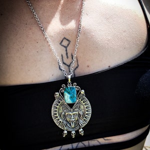 May include: A silver necklace with a large pendant featuring a turquoise stone and a detailed silver skull design.
