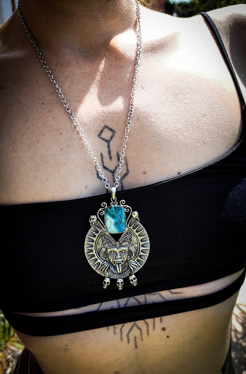 May include: A silver necklace with a large pendant featuring a turquoise stone and a detailed silver skull design.