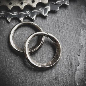 May include: Two silver metal rings on a black surface. The rings are smooth and have a slightly textured finish.