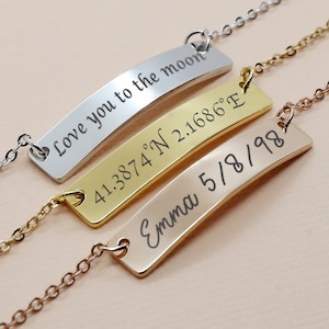 May include: Three silver, gold, and rose gold necklaces with engraved nameplates. The silver necklace has the text "Love you to the moon". The gold necklace has the text "41.3874°N 2.1686°E". The rose gold necklace has the text "Emma 5/8/98".