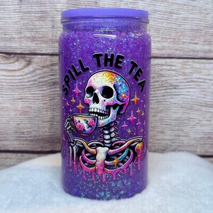 May include: A purple glitter tumbler with a matching lid. The tumbler features a colorful skeleton graphic holding a teacup, with the words "Spill The Tea" in black. The design includes stars and dripping paint effects.