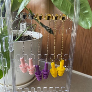 May include: Four pairs of earbud style earrings with different colored silicone tips. The earrings are silver, gold, and two different shades of gold. The silicone tips are pink, purple, and yellow.