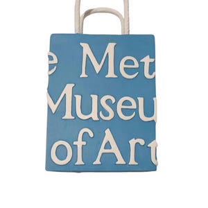May include: A blue shopping bag with white handles and the text "The Met Museum of Art" printed on the front.
