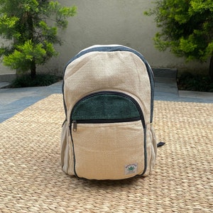 May include: A beige hemp backpack with a green hemp pocket and a black zipper. The backpack has a small green leaf logo with the text "WORLD WIDE WEBB" on it.