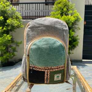 Könnte beinhalten: Ein grauer, grüner und brauner Hanfrucksack mit einer Reißverschlusstasche und einem Patch mit der Aufschrift "Hemp Planet" mit einem grünen Blattlogo.