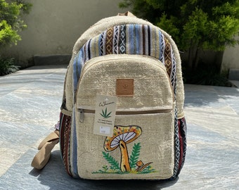 May include: Beige backpack with a mushroom design. The backpack has a front pocket with a zipper, adjustable straps, and a top handle. The mushroom is orange, yellow, and white with green leaves. The backpack has a woven pattern.