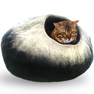 May include: A black and white felt cat bed shaped like a large, smooth stone. A tabby cat is peeking out of the opening.