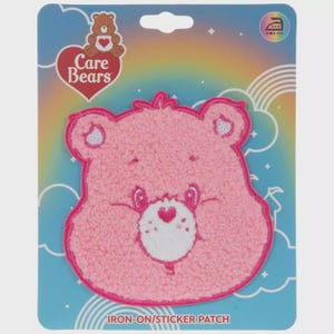 May include: A pink Care Bear iron-on/sticker patch. The patch features a pink Care Bear face with a white heart-shaped nose and a pink outline. The patch is on a blue and rainbow-colored background with the words "Care Bears" and "Iron-On/Sticker Patch".