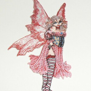 May include: Embroidered patch of a fairy with red and white wings and a pink dress. The fairy has blonde hair and is wearing striped stockings. The patch is detailed with various colors and textures.
