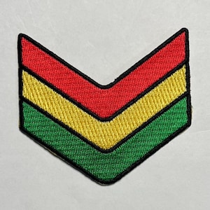 May include: A colorful embroidered patch in a chevron design. The patch features three horizontal stripes in red, yellow, and green, outlined with a black border. The patch is likely for clothing or accessories.