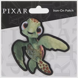 May include: An iron-on patch featuring a cartoon sea turtle character with large eyes and a friendly expression. The patch is green, with a black border, and the Pixar logo is visible at the top.