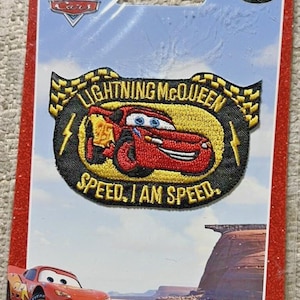 May include: A Disney Pixar Cars embroidered patch featuring Lightning McQueen on a yellow oval background with black borders. The text reads LIGHTNING MCQUEEN and SPEED. I AM SPEED. The patch is mounted on a branded cardboard backing card.