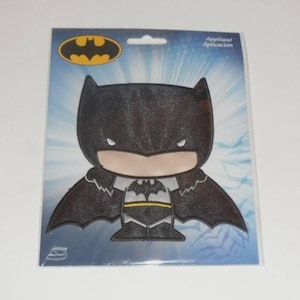 May include: A Batman applique patch in a package. The patch features a cartoon-style Batman with a black and gray color scheme. The packaging has a blue background with the Batman logo in yellow.